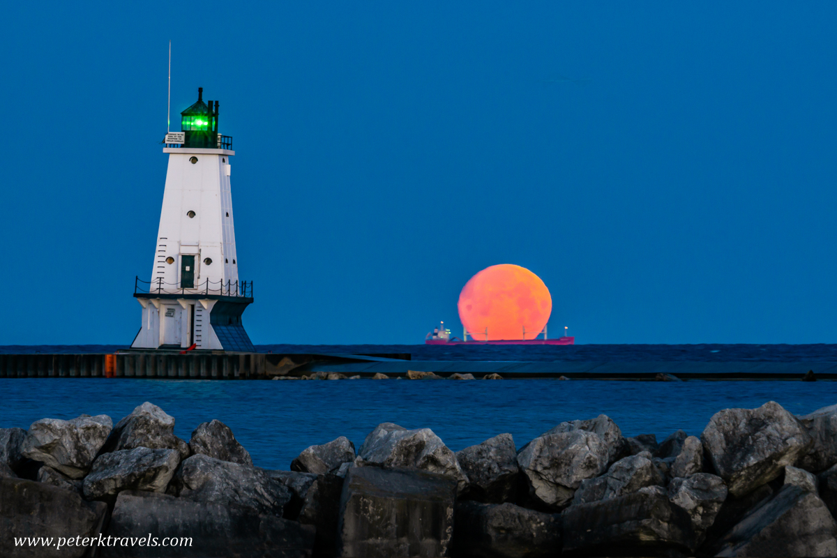 A setting moon and ore carrier, with the Ludington Lighthouse.